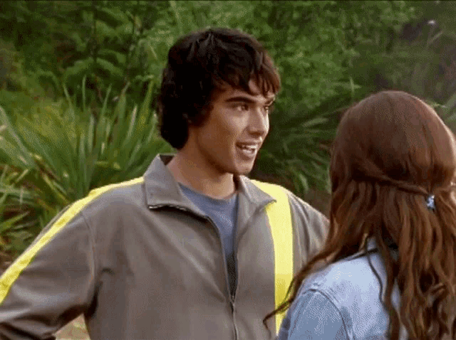 a man and a woman are standing next to each other and the man is wearing a grey jacket with yellow stripes