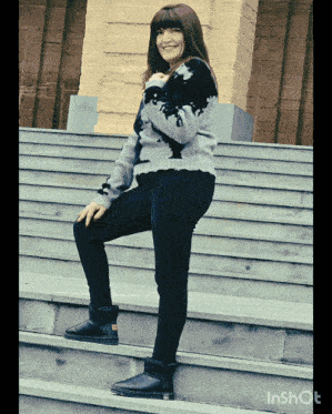 a woman wearing a sweater and black pants is standing on a set of steps