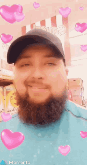 a man with a beard wearing a hat and surrounded by pink hearts says momento