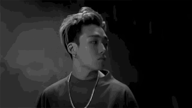 a black and white photo of a young man wearing a necklace and earrings .