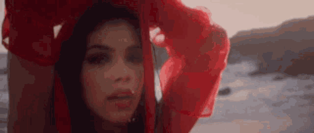 a woman in a red dress is standing on a beach with a red scarf covering her head .