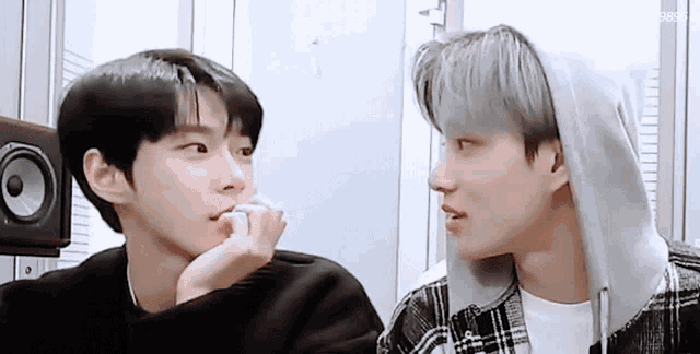 two young men are looking at each other in a room and one of them is wearing a hoodie .