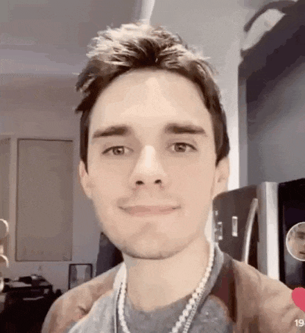 a young man is wearing a pearl necklace and smiling .