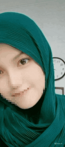 a woman wearing a green hijab is smiling in front of a wall clock