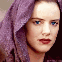 a woman with blue eyes is wearing a purple scarf around her head .