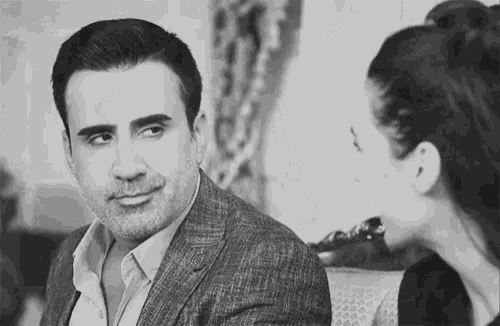 a man in a suit and a woman in a ponytail are sitting next to each other in a black and white photo .
