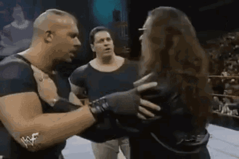 a man is hugging a woman in a wrestling ring while two other men watch .