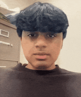 a young man with blue hair and a black shirt looks at the camera