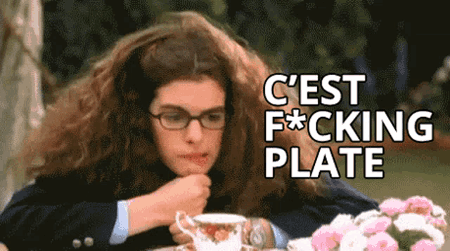 a woman with glasses sits at a table with flowers and says " c'est fucking plate "