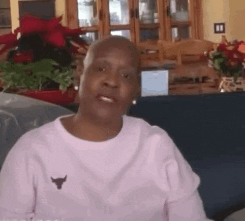 an older woman is sitting on a couch wearing a pink shirt with a bull on it .
