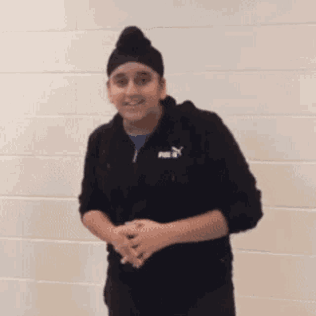 a young man wearing a turban and a black puma hoodie is dancing in front of a white wall .