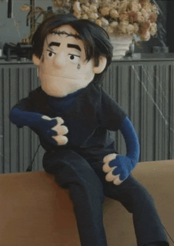 a puppet with a black shirt and blue gloves is sitting on a couch