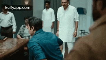 a man in a blue shirt is sitting at a table talking to another man .