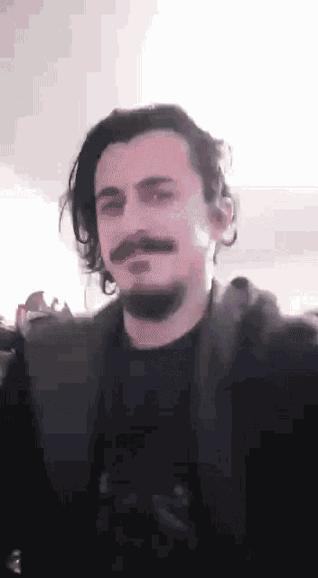 a man with a beard and long hair is wearing a black shirt and a black jacket .