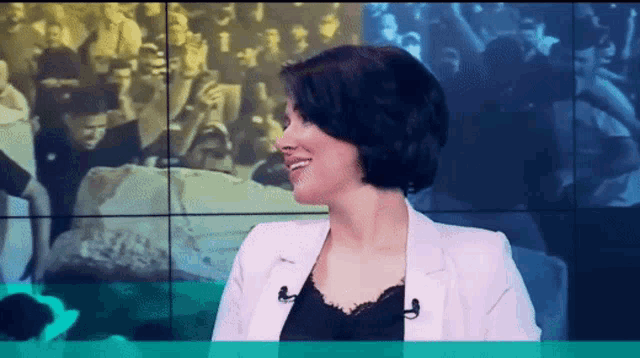 a woman is smiling in front of a crowd on a television screen