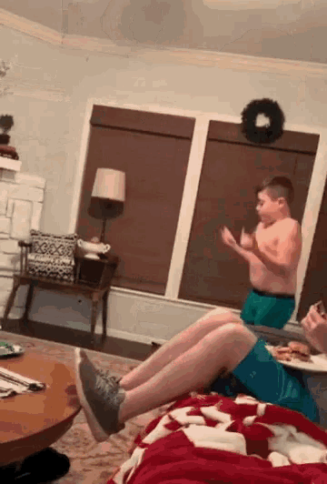 a shirtless boy in green under armour shorts is sitting on a couch in a living room