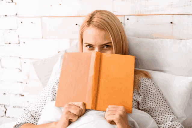 a woman laying in bed with a book in front of her face