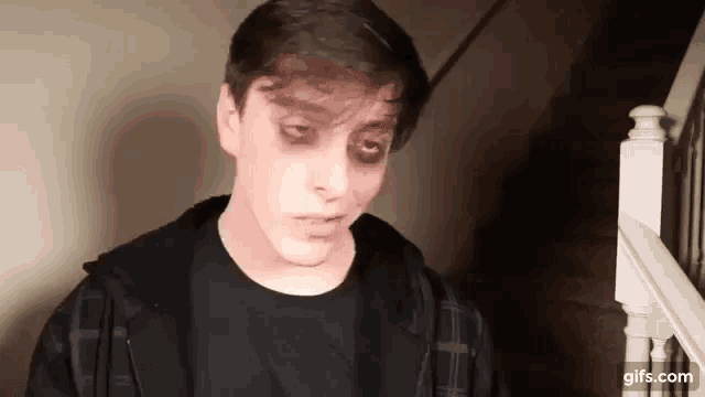 a young man with black eyes and a black shirt is standing in front of a staircase .