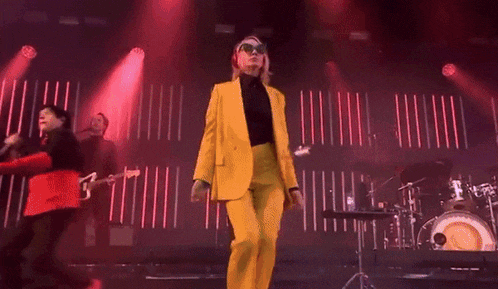 a woman in a yellow suit and sunglasses is dancing on stage