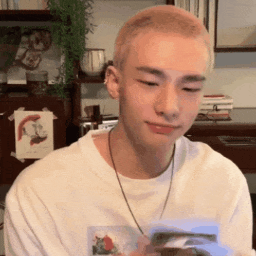 a young man with blonde hair is wearing a white shirt and a necklace .
