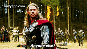 thor is standing in the middle of a field with a group of people in the background and asking anyone else .