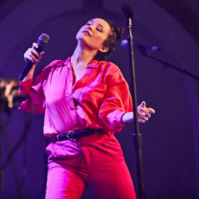 a woman singing into a microphone while wearing a pink shirt
