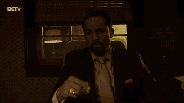 a man in a suit and tie is sitting in front of a screen that says beta
