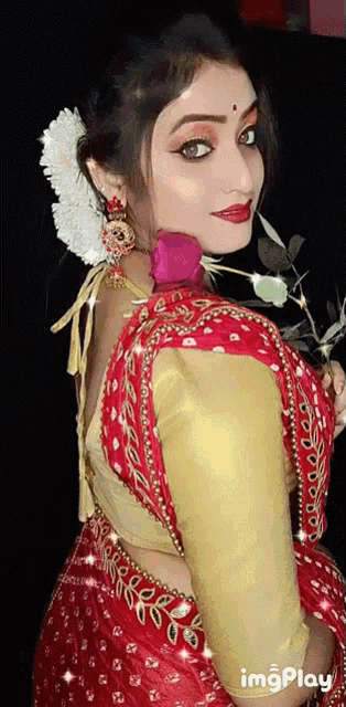 a woman in a red and gold dress is holding a pink rose in her hand