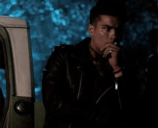 a man in a leather jacket is smoking a cigarette in the dark