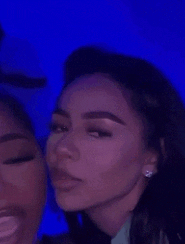a woman is whispering into another woman 's ear while wearing a glow in the dark necklace .