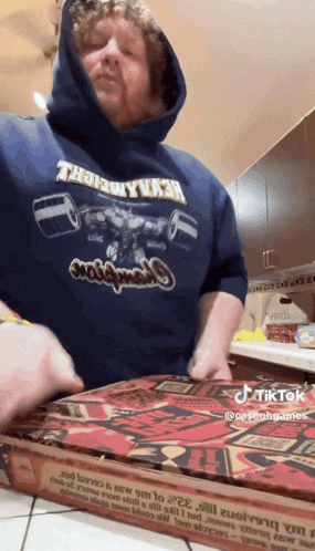 a man wearing a hoodie that says thank you is opening a pizza box in a kitchen