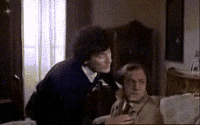 two men are sitting on a couch talking to each other in a room