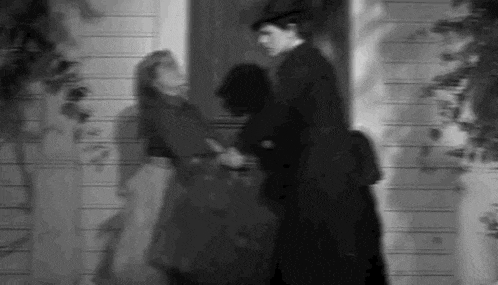 a black and white photo of a man and a woman standing next to each other in front of a house .