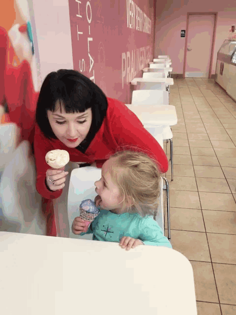 a woman in a red sweater holds an ice cream cone next to a little girl in a green shirt