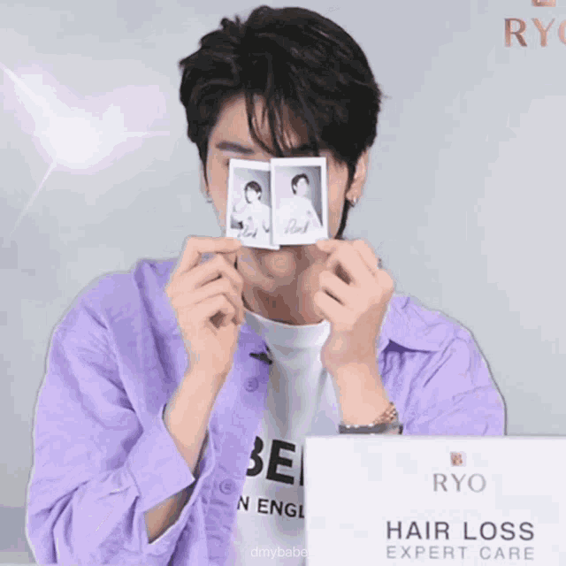 a man in a purple shirt is holding a polaroid picture in front of his face in front of a sign that says ryo
