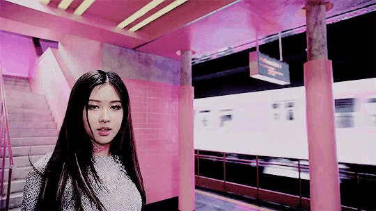 a woman is standing in a subway station with a train coming down the tracks .