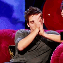 a man covering his face with his hands while sitting on a pink couch