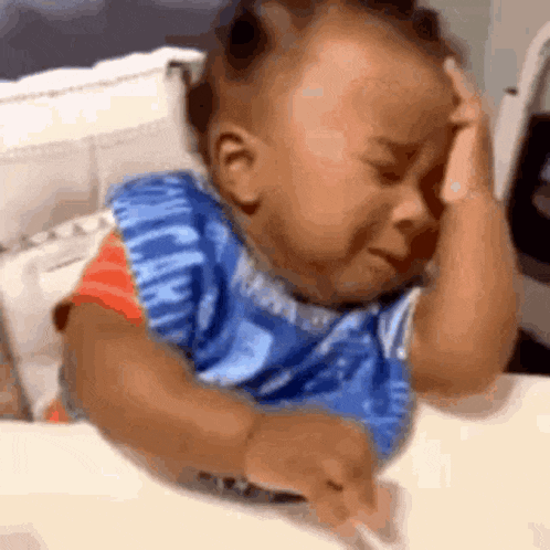 a baby is crying while sitting at a table with his hands on his head .