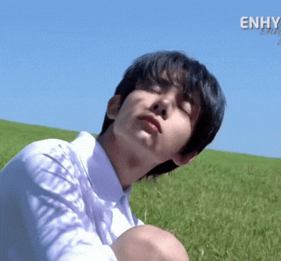 a young man in a white shirt is sitting in a field of grass with his eyes closed .