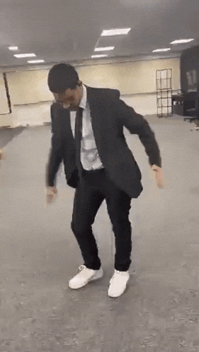 a man in a suit and tie is dancing in a room while wearing white sneakers .