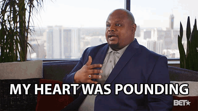 a man in a suit sits on a couch with the words my heart was pounding behind him
