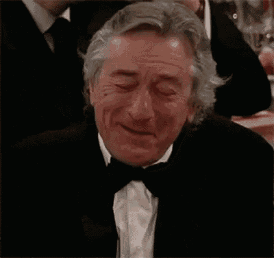 a man in a tuxedo and bow tie is laughing while sitting at a table .