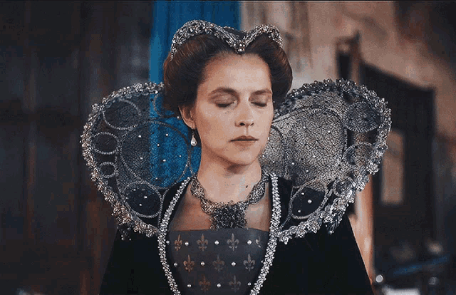 a woman in a costume with a large collar and a necklace with fleur de lis on it