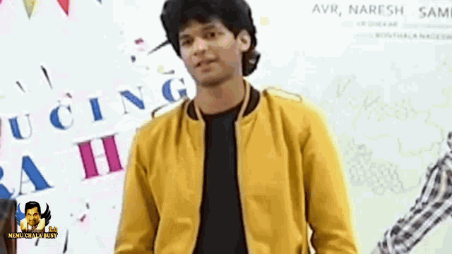 a young man wearing a yellow jacket is standing in front of a movie poster .