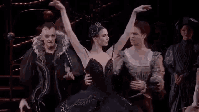 a ballerina in a black dress is dancing on a stage with two other dancers .