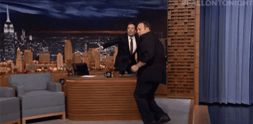 two men are dancing in front of jimmy fallon 's desk on the tonight show
