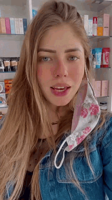 a woman wearing a floral face mask and a denim jacket looks at the camera