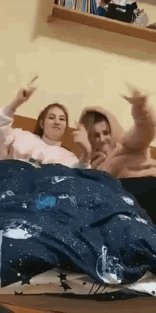 two girls are laying on a bed with a blanket that has space on it