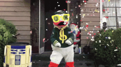 a duck mascot is dancing in front of a house while confetti is falling from the sky .