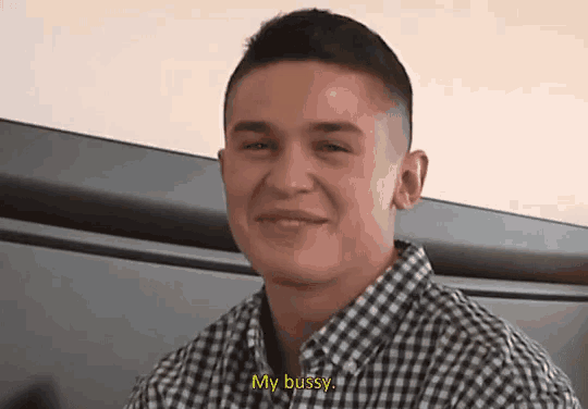 a man in a plaid shirt is smiling and says " my busy "